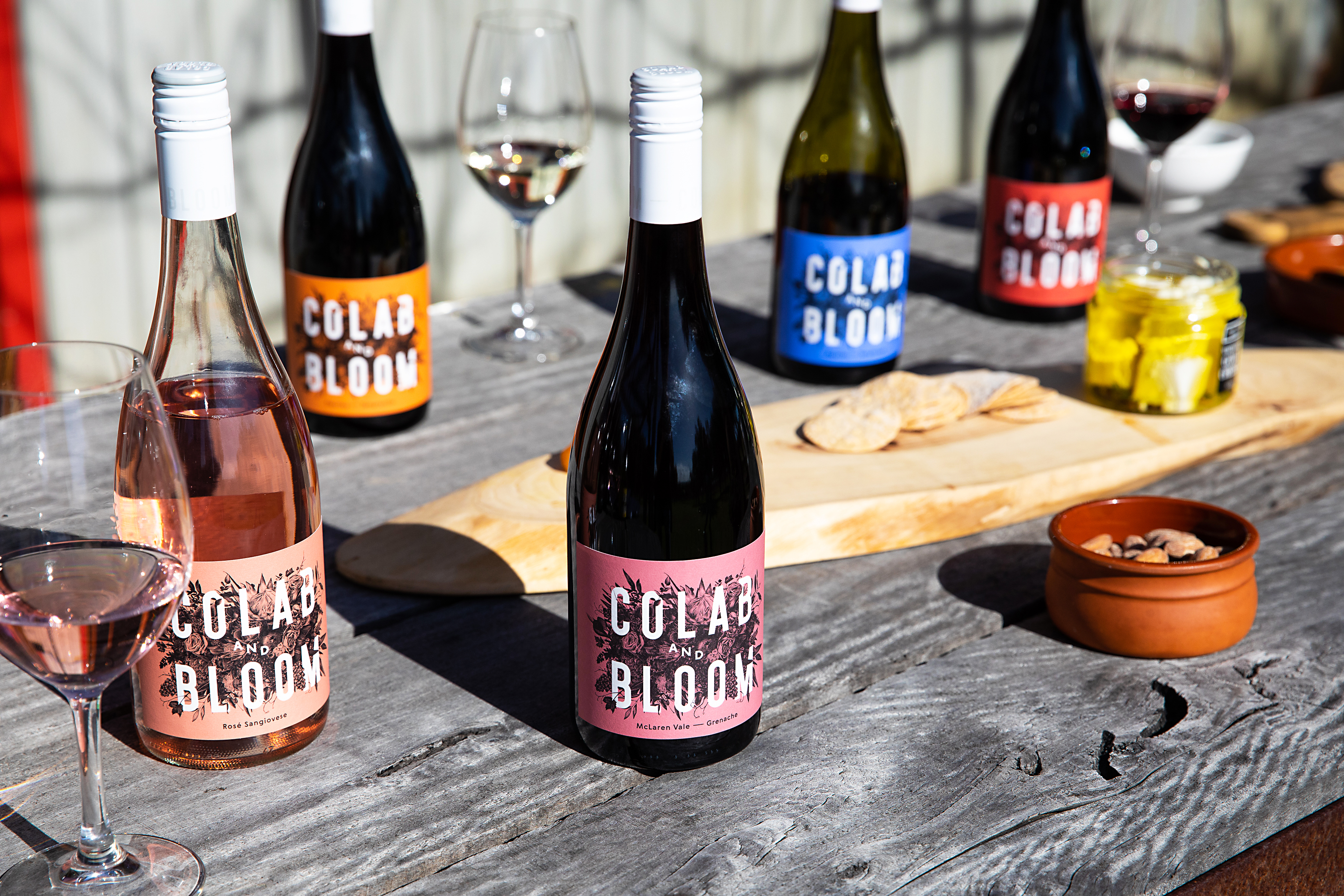 Five bottles of Colab and Bloom wines with cheese plate on a table